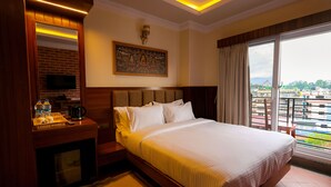 A hotel room with a large bed, a television on a wooden cabinet, a painting on the wall, and a view of the city through the window. - Boudha Boutique Inn (Kathmandu)