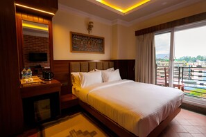 A hotel room with a large bed, a television on a wooden cabinet, a painting on the wall, and a view of the city through the window. - Boudha Boutique Inn (Kathmandu)