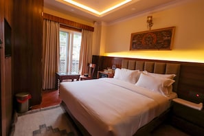 Una habitación de hotel con una cama grande, una mesita de noche, un escritorio con silla, una ventana con cortinas y una obra de arte colgada en la pared.