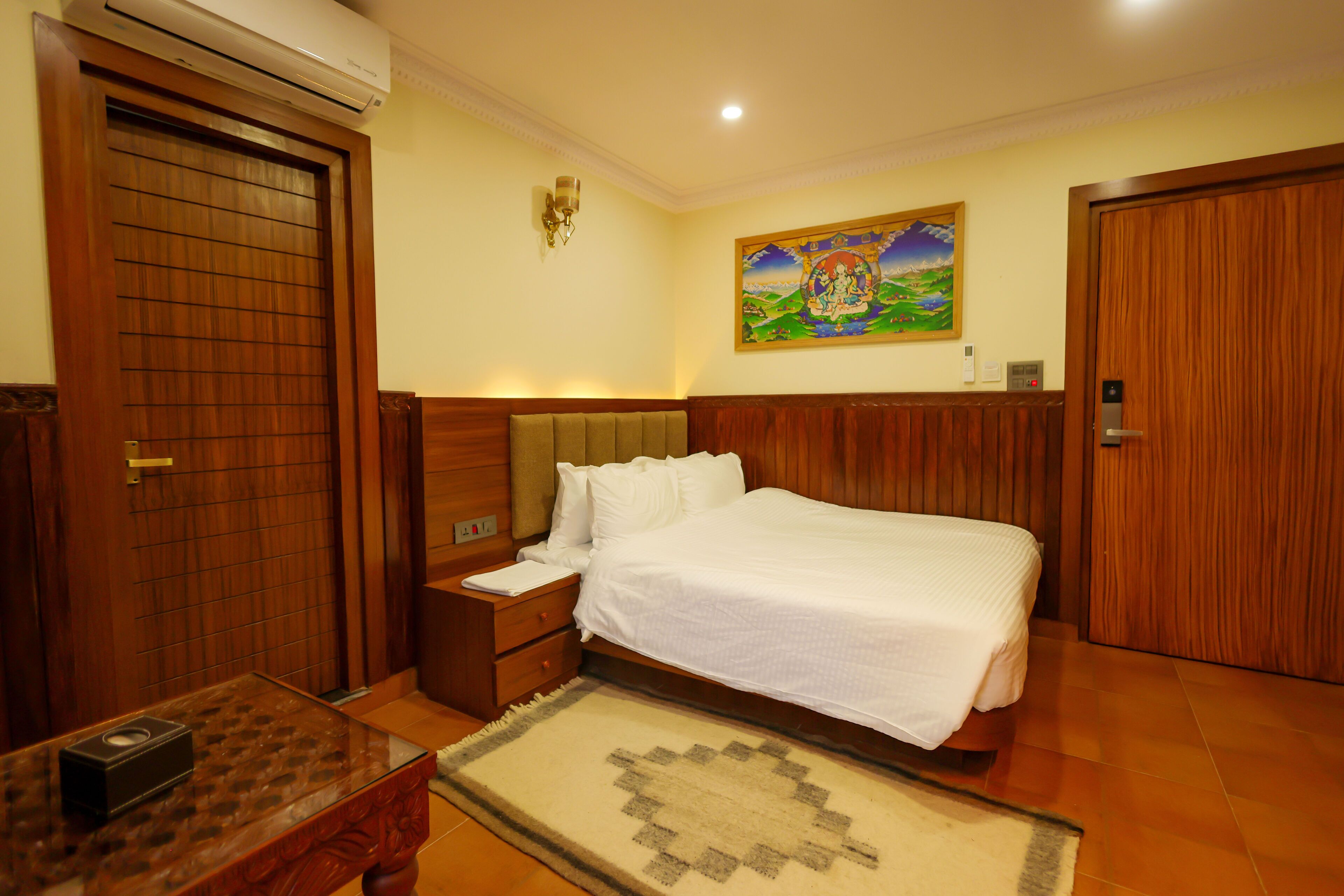 A hotel room with a wooden bed, nightstand, and a wall-mounted air conditioner.