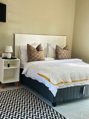 Quarto bem arrumado com cama, mesa de cabeceira, abajur e tapete estampado.