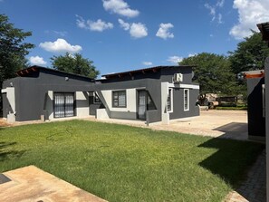 Uma casa moderna de dois andares com telhado plano, varanda coberta e gramado bem cuidado.