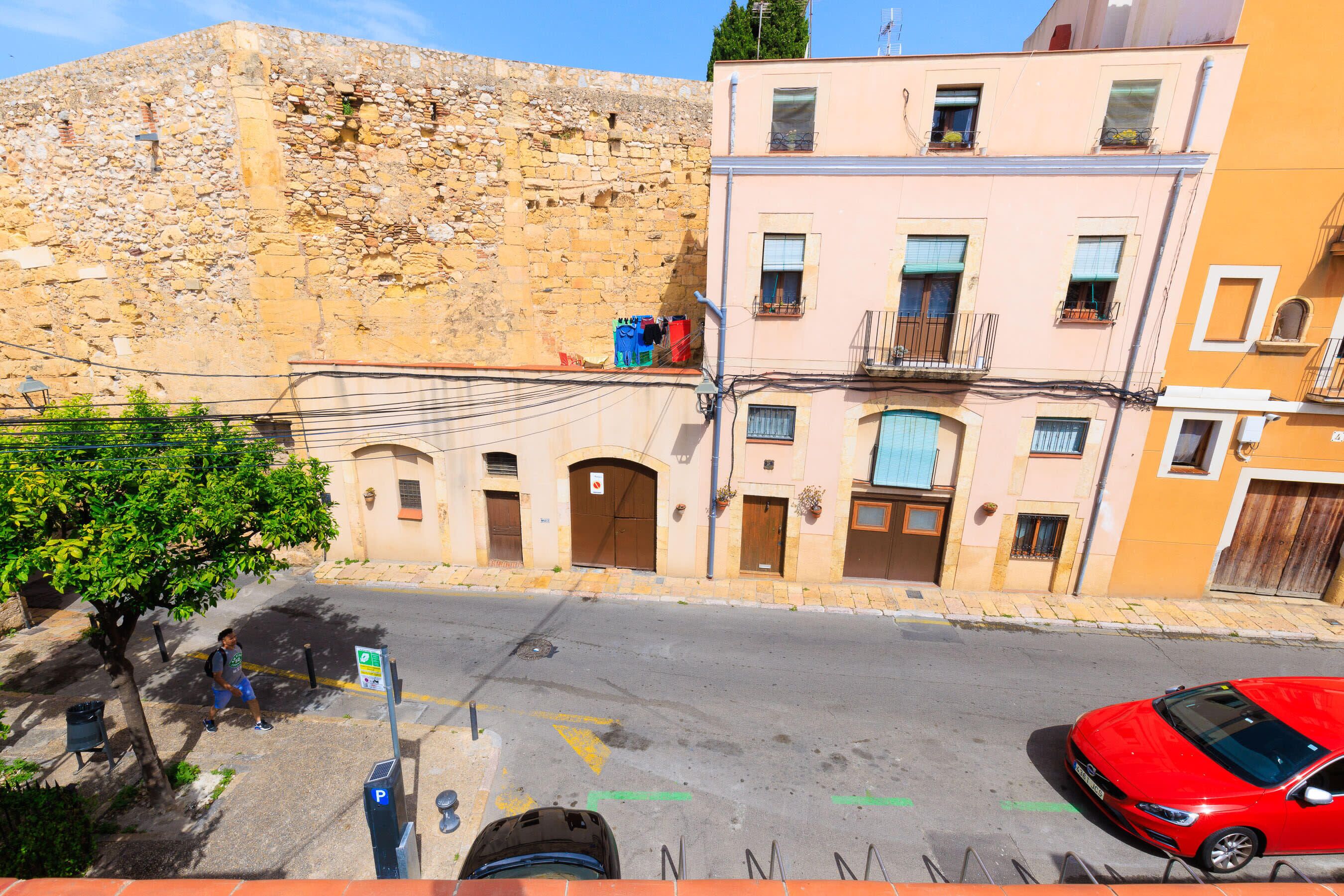 A street with buildings, a red car, and a person walking.