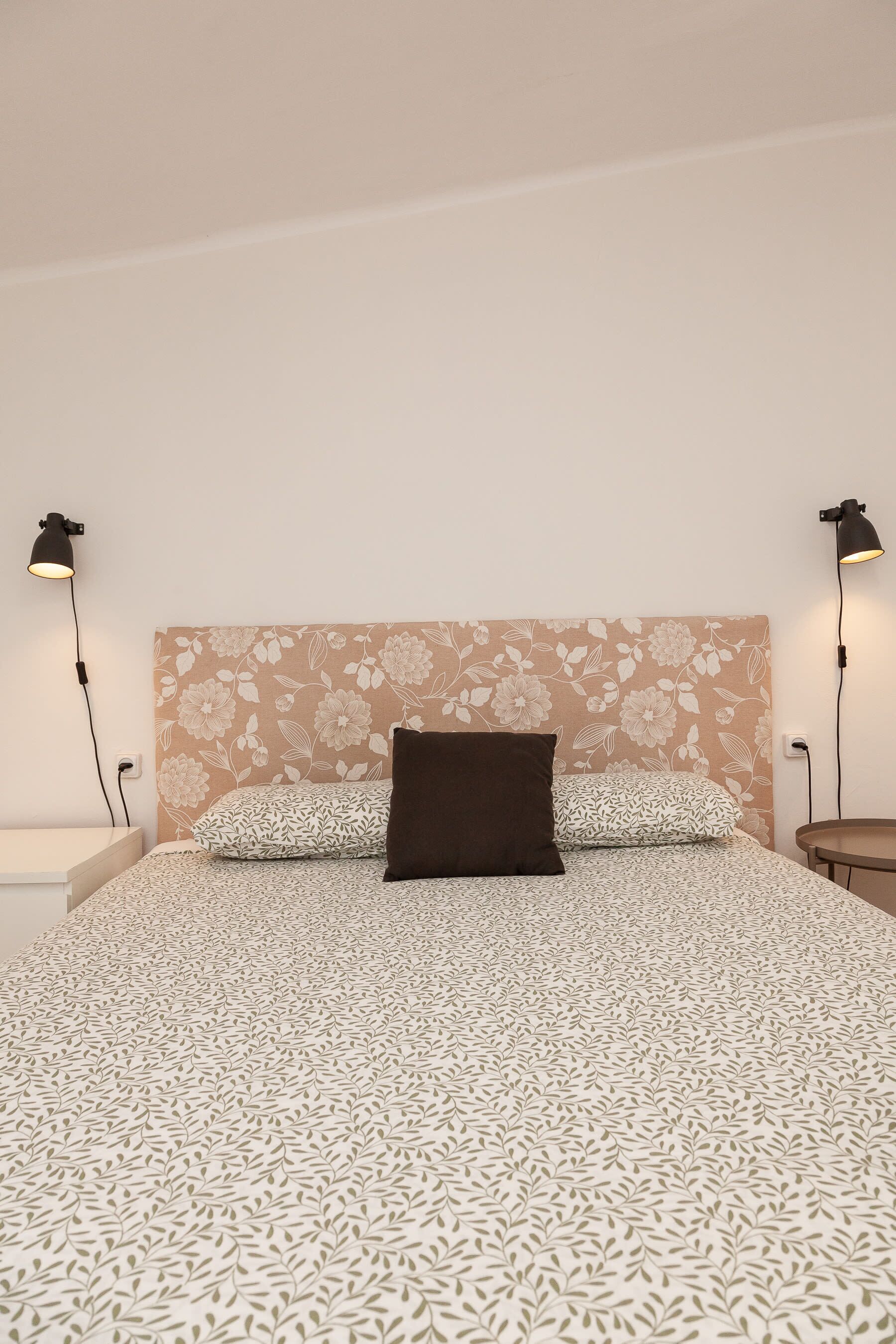 A bed with patterned bedding, a floral headboard, and two bedside lamps.