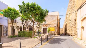 A narrow street with stone buildings, trees, bollards, and a yellow sign. - Part Alta • Sant Joan - Unik Vacation (Tarragona)