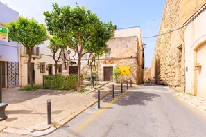 Una calle estrecha con edificios de piedra, árboles, pilares y un letrero amarillo.