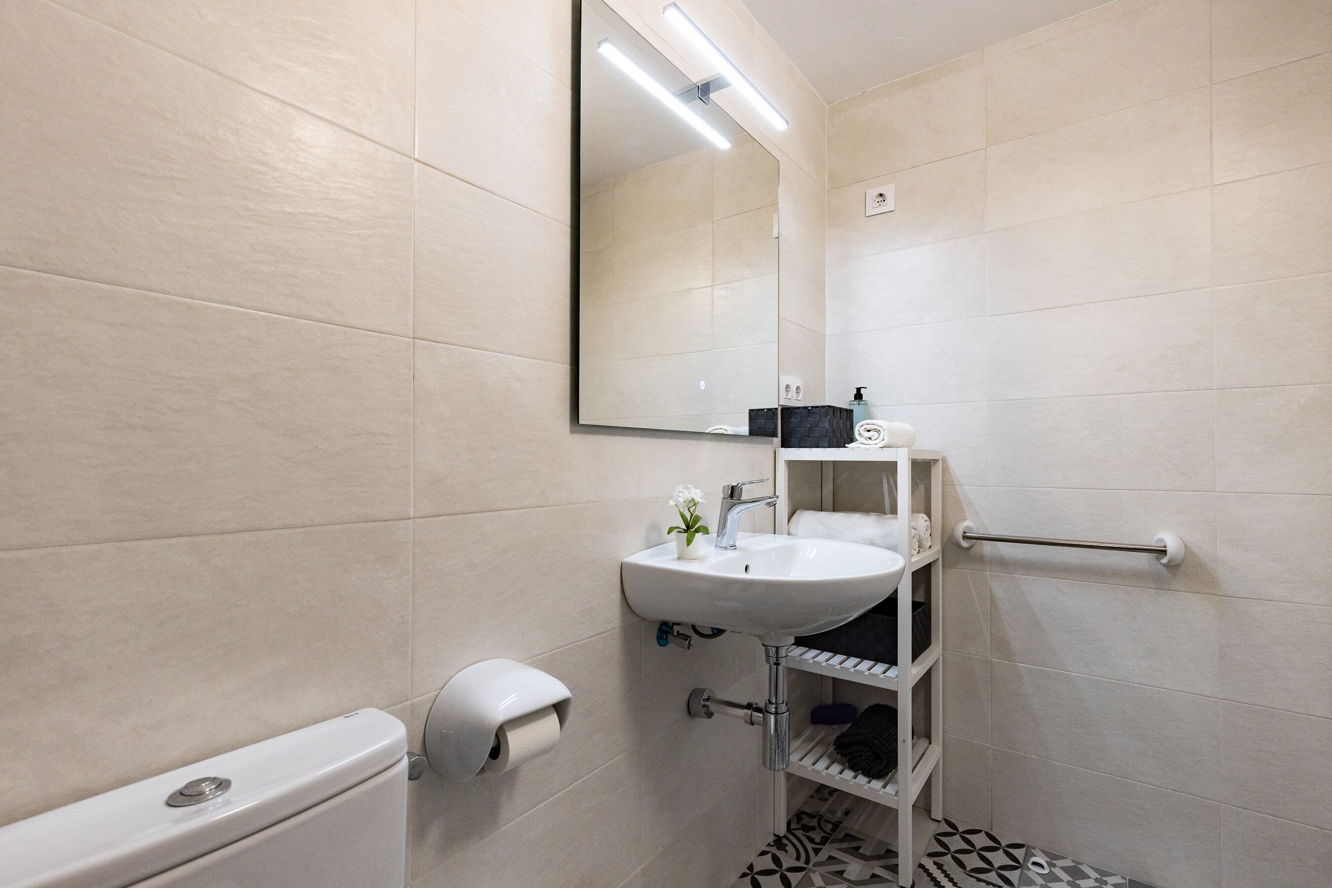 Un baño moderno con inodoro, lavabo, espejo, toallero y dispensador de papel higiénico.