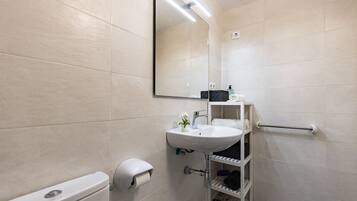 Un baño moderno con inodoro, lavabo, espejo, toallero y dispensador de papel higiénico.