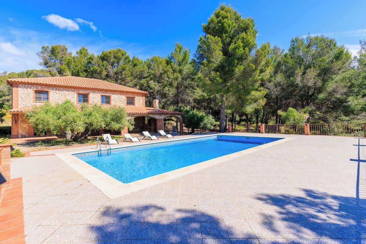 A pool with lounge chairs, a stone building, and trees in the background.