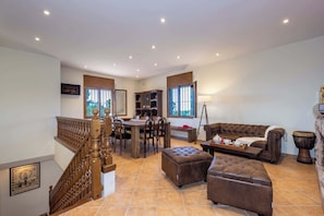 A spacious living area with a staircase, a dining table, a sofa, and a fireplace.