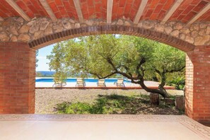 An outdoor patio area with a brick archway, a tree, and a pool with lounge chairs. - Masia Garriga (Tarragona)