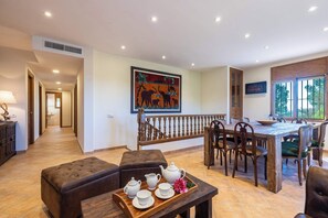 A spacious dining area with a wooden table and chairs, a bench with a tray of tea set, and a staircase with a railing.