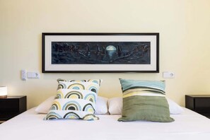 Une chambre d’hôtel avec un lit, deux tables de chevet, une œuvre d’art encadrée au-dessus du lit et une prise électrique au mur.