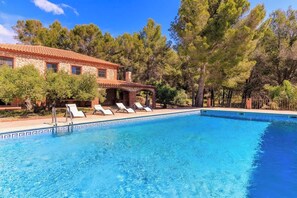 A swimming pool with lounge chairs, a stone building, and trees in the background.