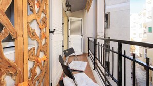 A balcony with a wooden decorative wall, a black chair, a white cushion, and a white door with shutters. - City Center · Ritort - Unik Vacation (Tarragona)