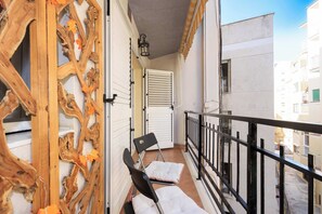 A balcony with a wooden decorative wall, a black chair, a white cushion, and a white door with shutters. - City Center · Ritort - Unik Vacation (Tarragona)