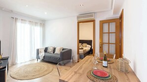 A modern living room with a sofa, a dining table set with plates and wine, and a large window with curtains. - City Center · Ritort - Unik Vacation (Tarragona)