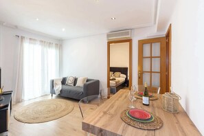 A modern living room with a sofa, a dining table set with plates and wine, and a large window with curtains. - City Center · Ritort - Unik Vacation (Tarragona)