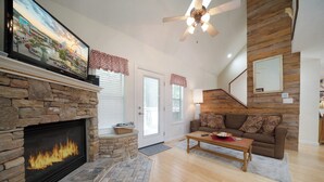 A living room with a stone fireplace, a ceiling fan, a couch, and a television. - Bear Cozy: Snuggle Up in the Smokies (Pigeon Forge)
