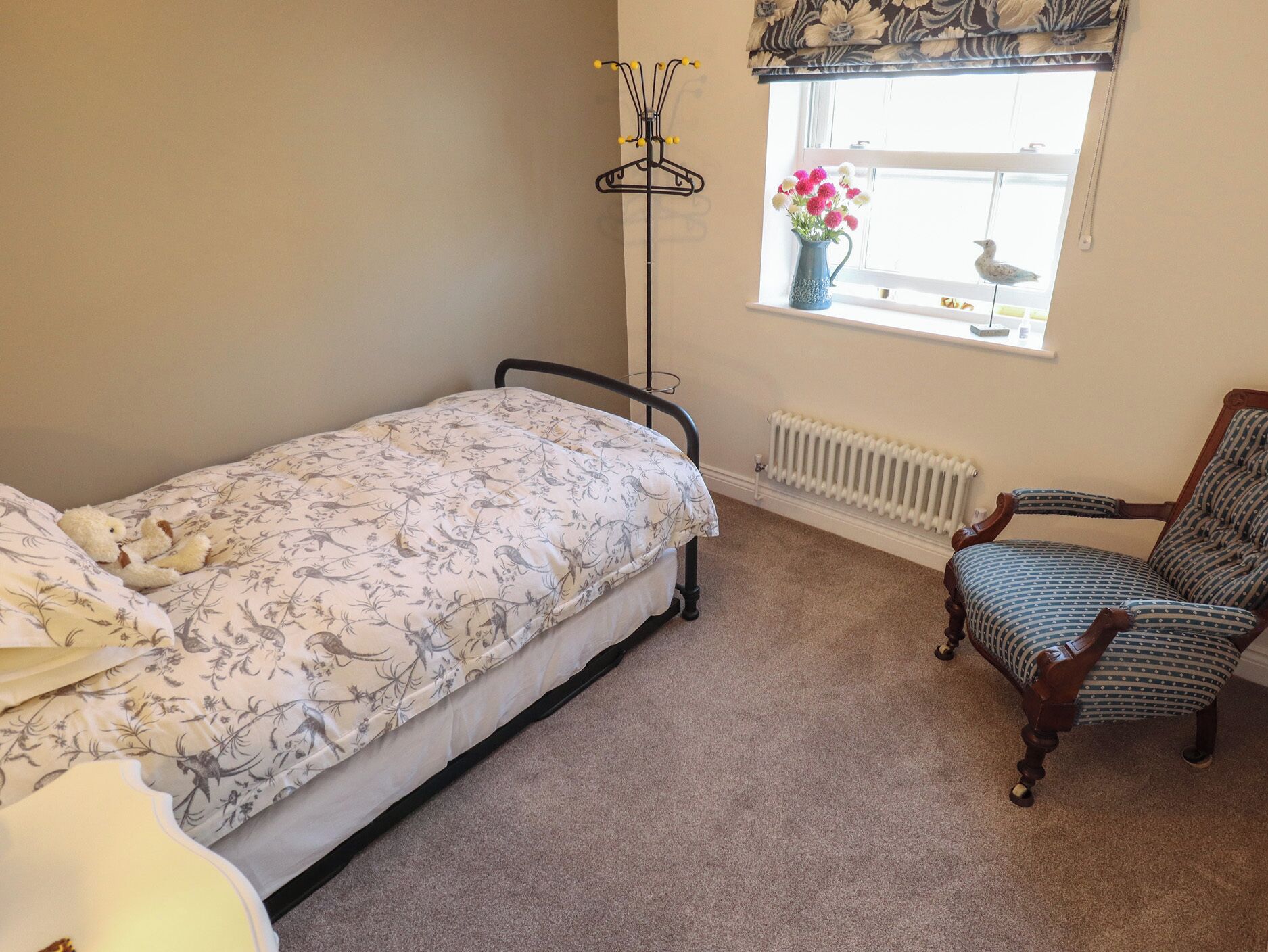 A bedroom with a single bed, a chair, a radiator, and a window with a curtain.