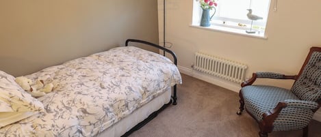 A bedroom with a single bed, a chair, a radiator, and a window with a curtain.
