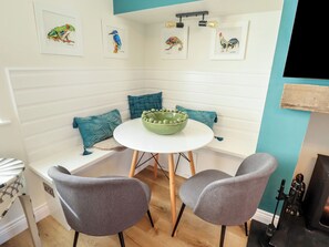 Eine Sitzecke mit einem runden Tisch, zwei grauen Stühlen, blaustichigen Kissen und Wandbildern.