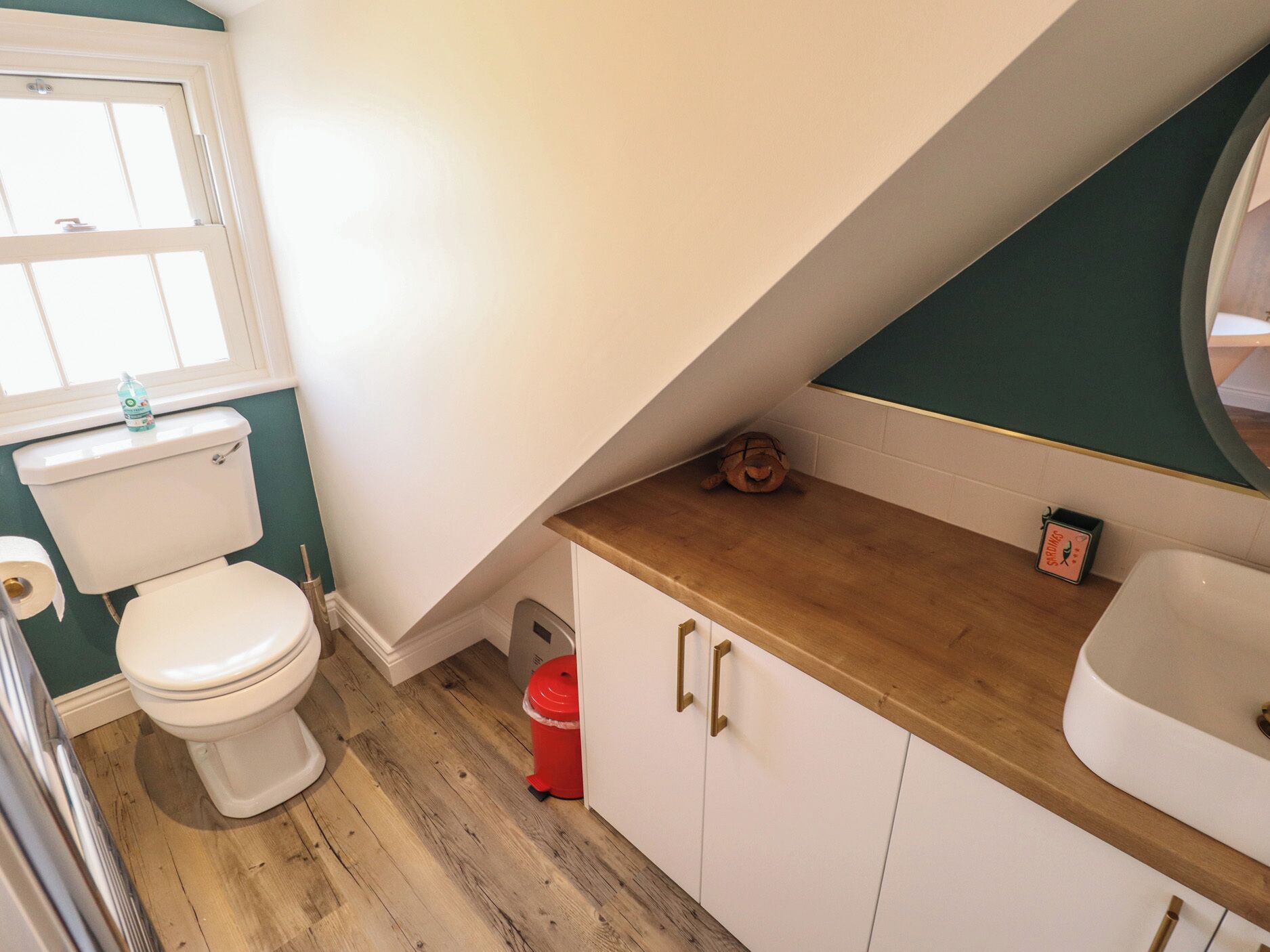 A bathroom with a toilet, a red trash bin, a wooden countertop, and a white sink.