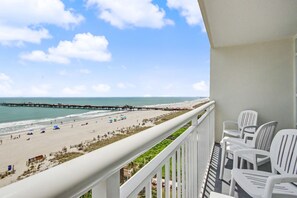 A balcony with white chairs, a view of the beach, and a pier extending into the water. - Oceanfront 2BR - 5th Floor w/ King & 2 Doubles + Breakfast for 2 + Lazy River (Myrtle Beach)