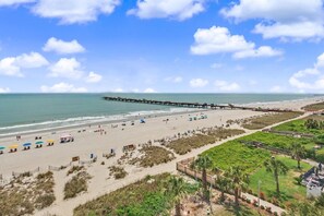 A beach with a pier extending into the water, umbrellas, and beach chairs. - Oceanfront 2BR - 5th Floor w/ King & 2 Doubles + Breakfast for 2 + Lazy River (Myrtle Beach)