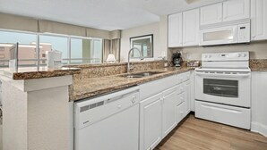 A modern kitchen with white cabinets, granite countertops, a built-in oven, and a microwave. - Oceanview 1BR Suite + Lazy River & Hot Tub (Myrtle Beach)
