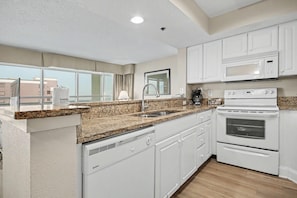 A modern kitchen with white cabinets, granite countertops, a built-in oven, and a microwave. - Oceanview 1BR Suite + Lazy River & Hot Tub (Myrtle Beach)