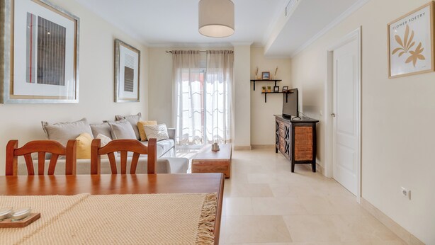 A living room with a dining table, chairs, a sofa, a TV stand, and a door. - LXR Atlantida 3-Bedroom Near the Ocean (Fuengirola)