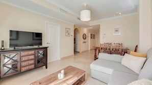 A living room with a flat-screen TV, wooden coffee table, sofa, dining table with chairs, and a hallway leading to a kitchen. - LXR Atlantida 3-Bedroom Near the Ocean (Fuengirola)