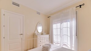 A bedroom with a bed, a dresser with a mirror, a door, and a window with curtains. - LXR Atlantida 3-Bedroom Near the Ocean (Fuengirola)