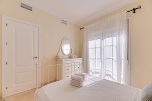 Ein Schlafzimmer mit Bett, Schminktisch mit Spiegel, einer Tür und einem Fenster mit Vorhängen.