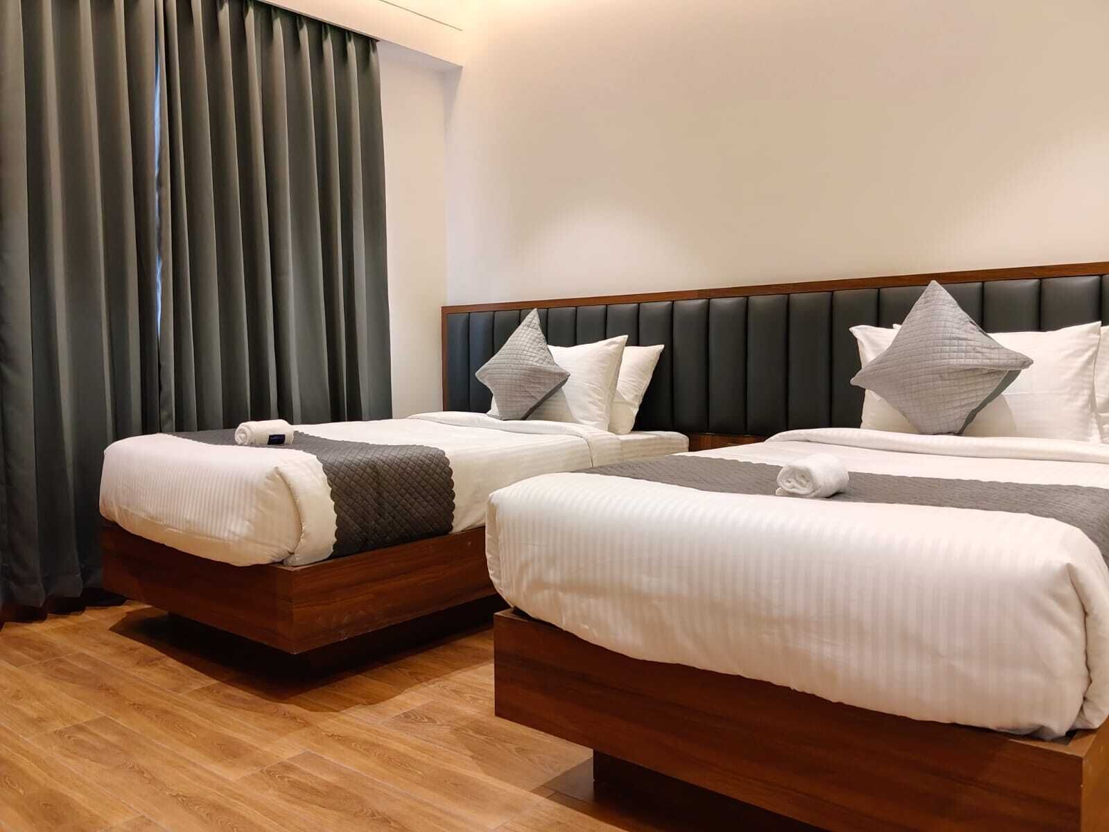 Ein Hotelzimmer mit zwei Betten, einem hölzernen Kopfteil und einem großen Fenster mit Vorhängen.