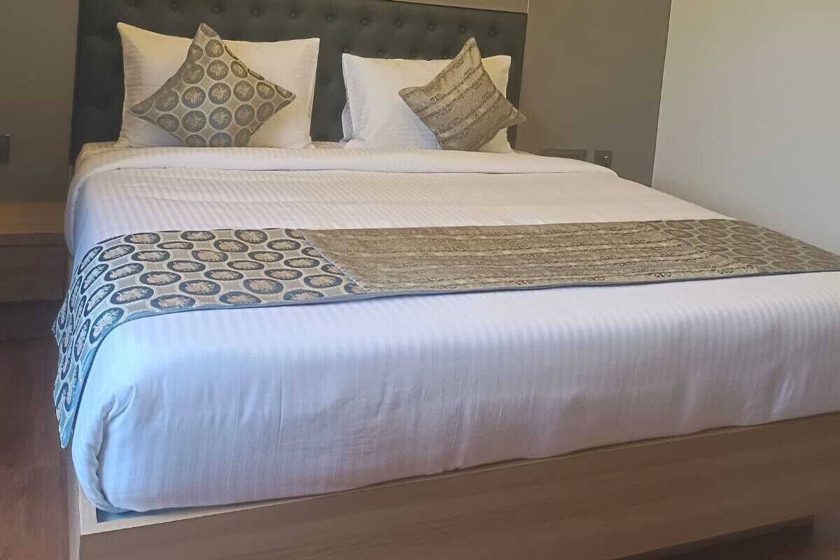 Moderni hotellihuone, jossa on suuri sänky, pyöreä kattovalaisin ja pelkistetty sisustus.