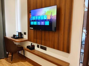 Habitació d'hotel moderna amb televisió de pantalla plana penjada a una paret de panells de fusta, escriptori de fusta amb una cadira i una petita banca.