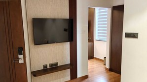 A hallway with a wooden floor, a mounted TV, and a door with a keycard lock. - LG CORDIAL (Mysore)