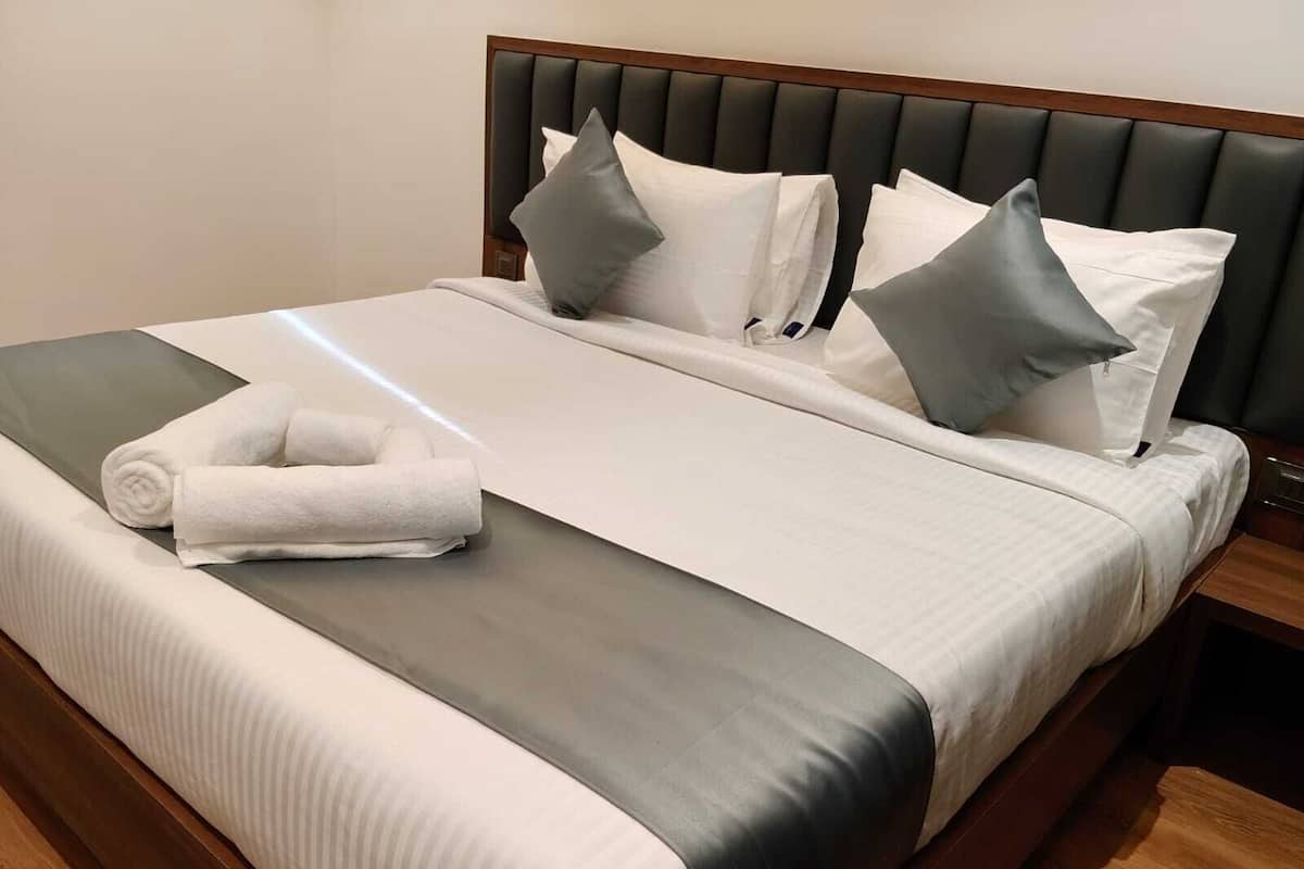 Una cama bien hecha con una colcha gris y blanca, un cabecero de madera y una mesita de noche a su lado.