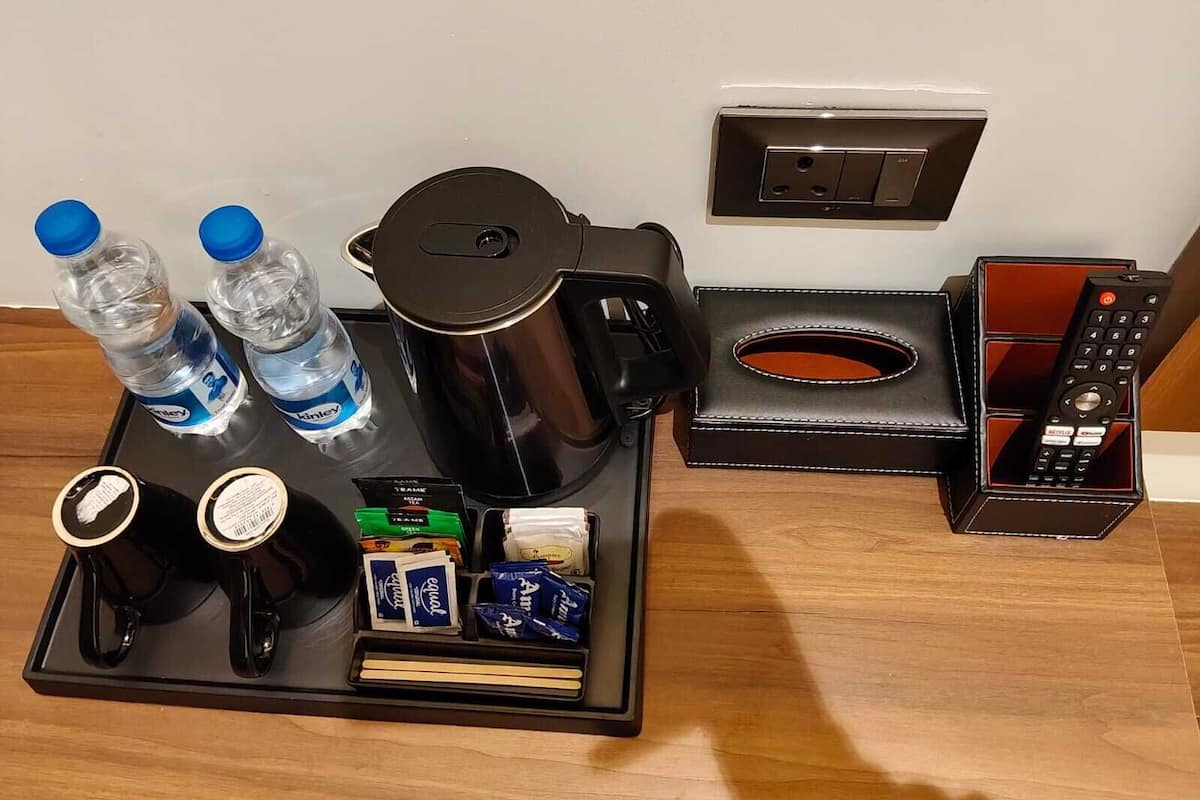 Minibar de una habitación de hotel con agua embotellada, café, té, aperitivos y un control remoto.