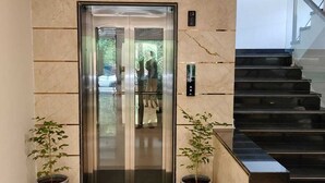 An elevator with a marble wall, a handrail, and two potted plants. - LG CORDIAL (Mysore)
