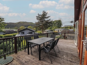A deck with a table and chairs, overlooking a residential area with houses and a forested hill. - Troutbeck Lodge (Keswick)