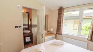A bedroom with a bed, a bathroom with a sink and mirror, and a window with curtains. - Troutbeck Lodge (Keswick)