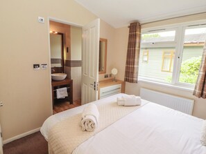 A bedroom with a bed, a bathroom with a sink and mirror, and a window with curtains. - Troutbeck Lodge (Keswick)