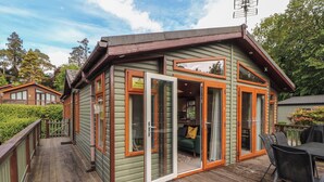 A wooden cabin with a deck, sliding glass doors, and a small outdoor seating area. - Troutbeck Lodge (Keswick)