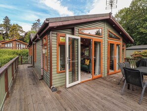 A wooden cabin with a deck, sliding glass doors, and a small outdoor seating area. - Troutbeck Lodge (Keswick)
