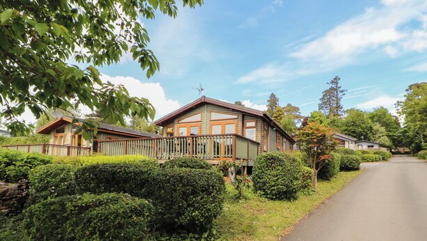 A two-story house with a balcony, surrounded by well-maintained hedges and a clear sky. - Troutbeck Lodge (Keswick)