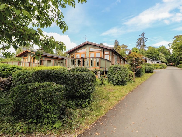 A two-story house with a balcony, surrounded by well-maintained hedges and a clear sky. - Troutbeck Lodge (Keswick)