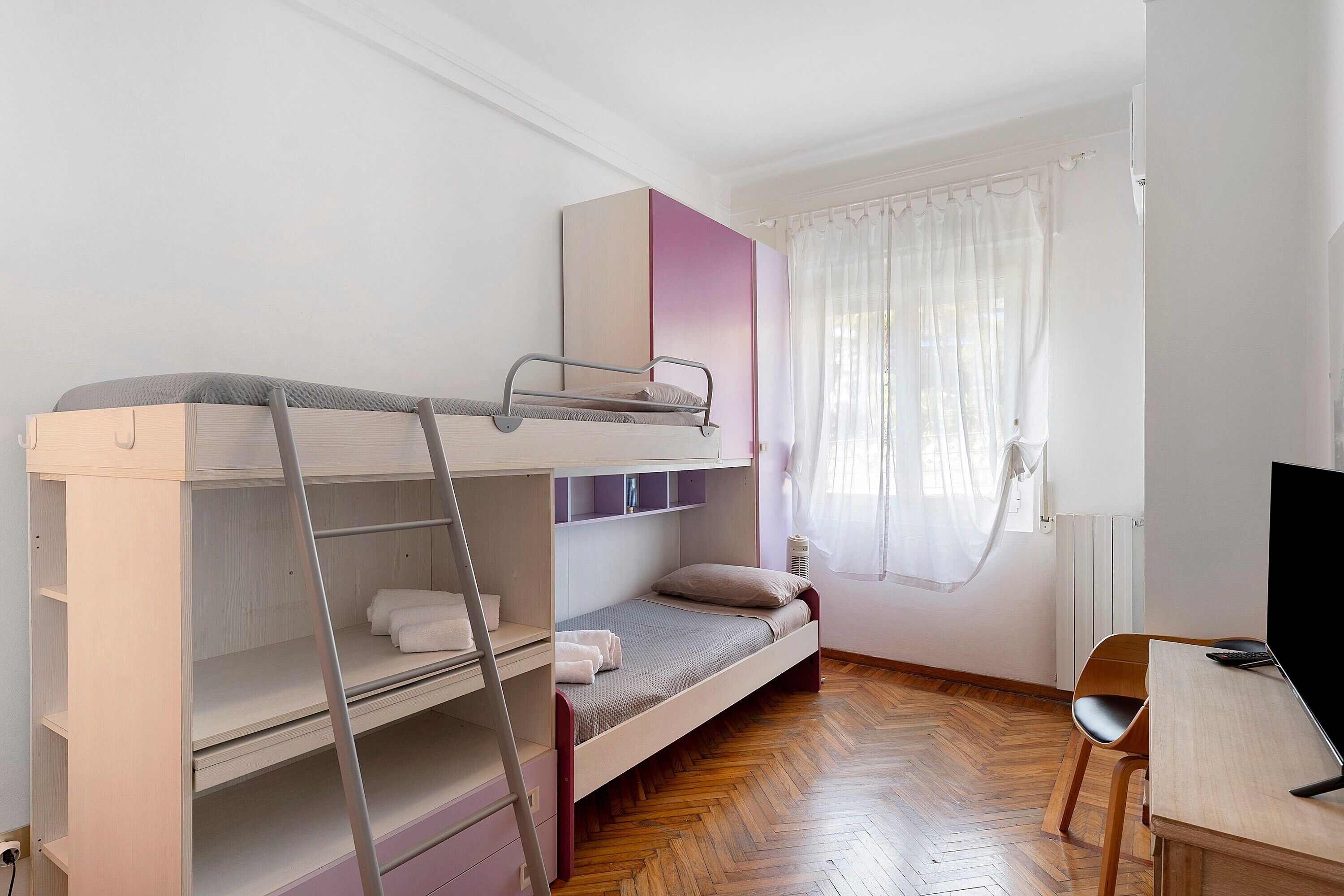 Una cama nido con una escalera, un escritorio con una silla y una ventana con cortinas.
